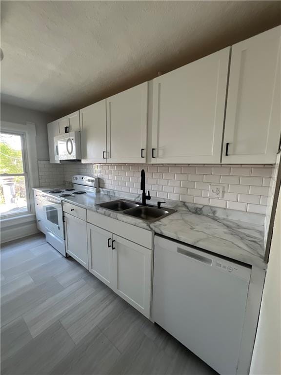 kitchen featuring light stone countertops, white appliances, backsplash, sink, and white cabinetry