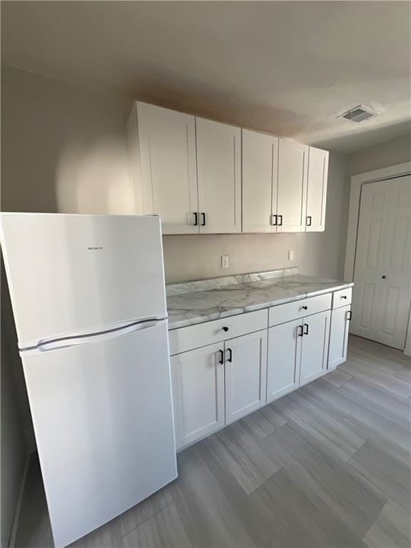 kitchen featuring white refrigerator, light stone counters, white cabinetry, and light hardwood / wood-style floors