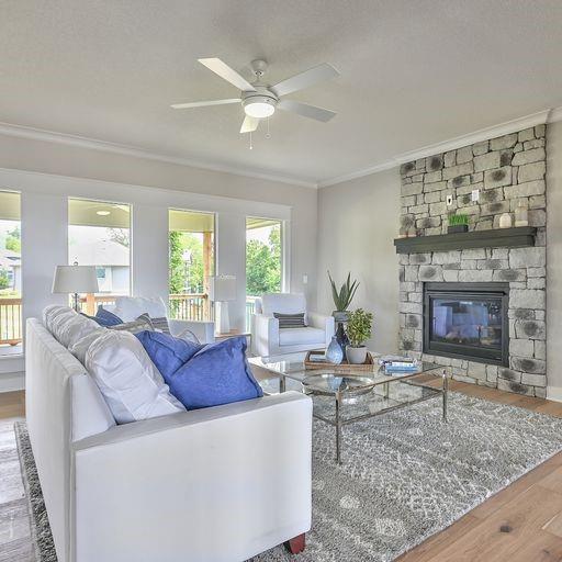 living room featuring a stone fireplace, crown molding, wood-type flooring, and ceiling fan