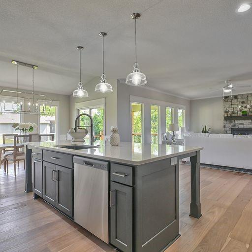 kitchen with a fireplace, dishwasher, a center island with sink, hanging light fixtures, and hardwood / wood-style flooring