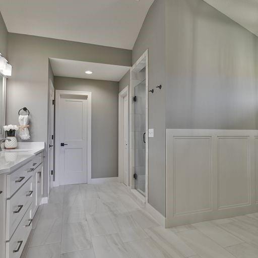 bathroom with tile flooring, a shower with shower door, lofted ceiling, and vanity