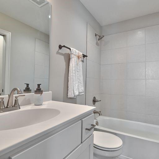 full bathroom with tiled shower / bath combo, toilet, and vanity with extensive cabinet space