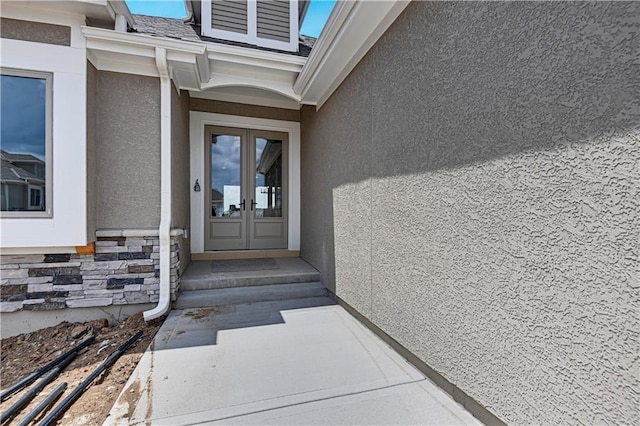 entrance to property with stone siding, french doors, and stucco siding