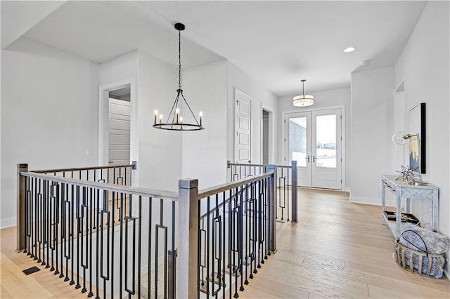 corridor featuring french doors, an upstairs landing, wood finished floors, a chandelier, and baseboards