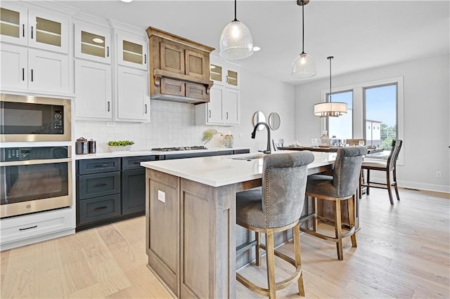 13028 S Constance St, Olathe, KS 66062 - kitchen featuring stainless steel appliances, decorative backsplash, light countertops, a kitchen island with sink, and light wood finished floors