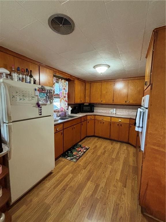 303 N Cayuga St, Frontenac, KS 66763 - kitchen featuring freestanding refrigerator, brown cabinets, light wood finished floors, a sink, and light countertops