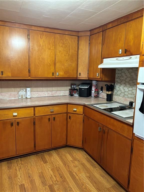 303 N Cayuga St, Frontenac, KS 66763 - kitchen with under cabinet range hood, brown cabinetry, decorative backsplash, light countertops, and light wood-style flooring