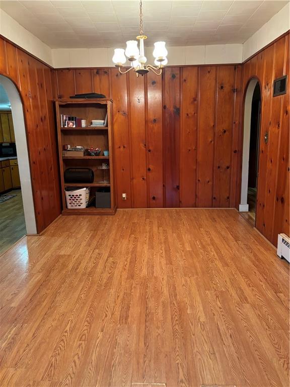 303 N Cayuga St, Frontenac, KS 66763 - unfurnished dining area featuring arched walkways, a chandelier, light wood-style flooring, and wooden walls