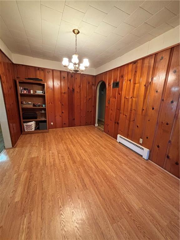 303 N Cayuga St, Frontenac, KS 66763 - unfurnished dining area with a baseboard radiator, arched walkways, light wood-type flooring, a chandelier, and wood walls