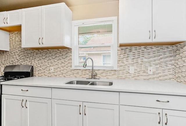 kitchen with stove, backsplash, sink, and white cabinetry