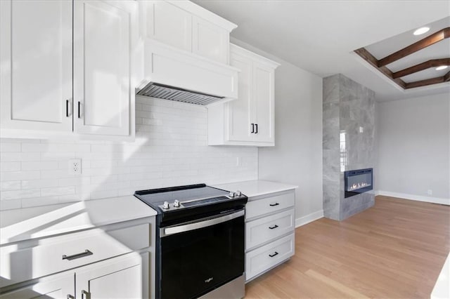 kitchen with light wood finished floors, tasteful backsplash, light countertops, a fireplace, and range with electric stovetop