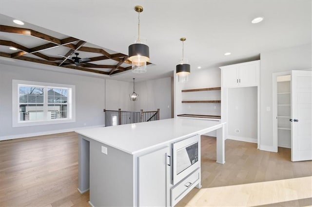 kitchen featuring light countertops, white microwave, white cabinetry, light wood-type flooring, and coffered ceiling