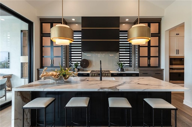 kitchen featuring hanging light fixtures, light stone countertops, stainless steel oven, and a spacious island