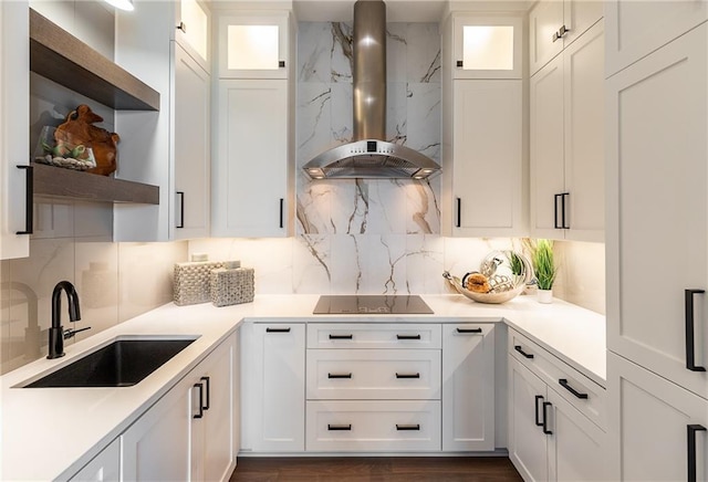 kitchen featuring wall chimney range hood, sink, backsplash, white cabinets, and black electric cooktop