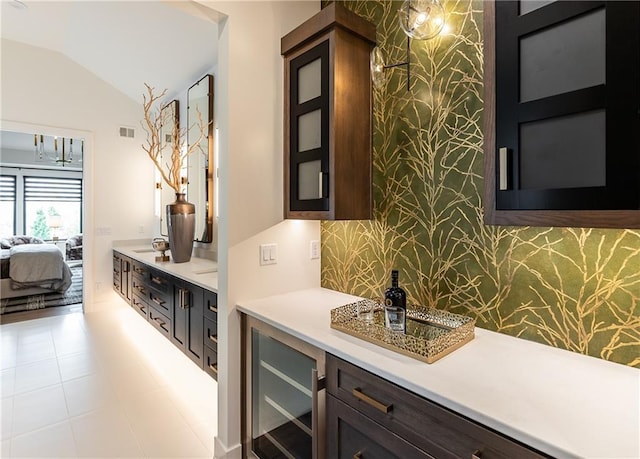 bar with backsplash, wine cooler, dark brown cabinetry, light tile patterned flooring, and vaulted ceiling