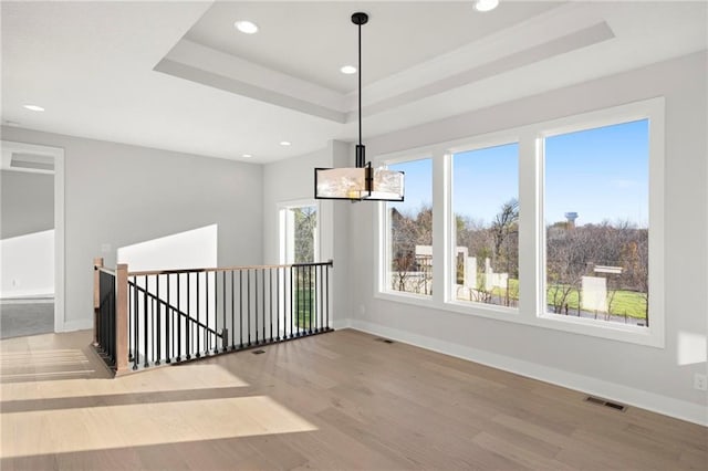 unfurnished dining area with a tray ceiling, an inviting chandelier, and hardwood / wood-style flooring