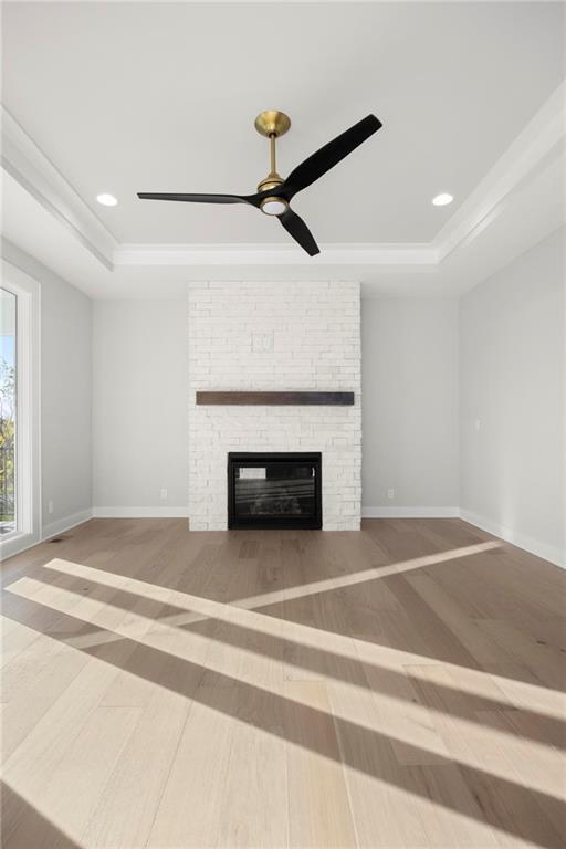 unfurnished living room featuring hardwood / wood-style flooring, a stone fireplace, and a tray ceiling