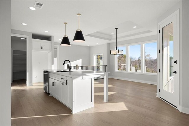 kitchen with sink, decorative light fixtures, light hardwood / wood-style flooring, white cabinets, and an island with sink