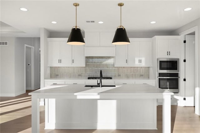 kitchen featuring light hardwood / wood-style floors, white cabinetry, an island with sink, and appliances with stainless steel finishes