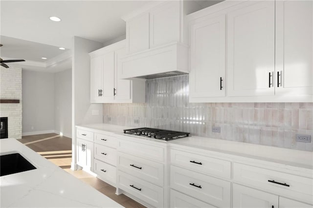 kitchen with backsplash, stainless steel gas stovetop, a fireplace, white cabinets, and light wood-type flooring