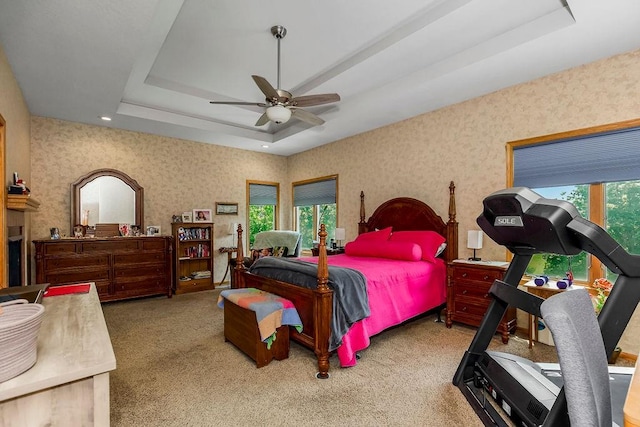 carpeted bedroom featuring a tray ceiling, ceiling fan, and multiple windows