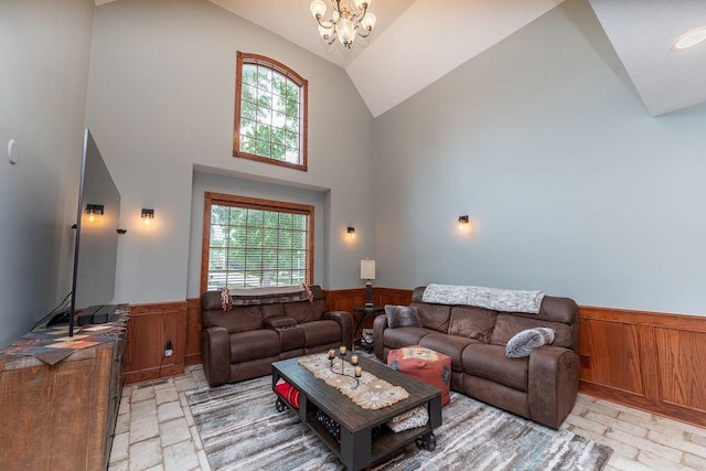 living room featuring high vaulted ceiling, wooden walls, and a chandelier