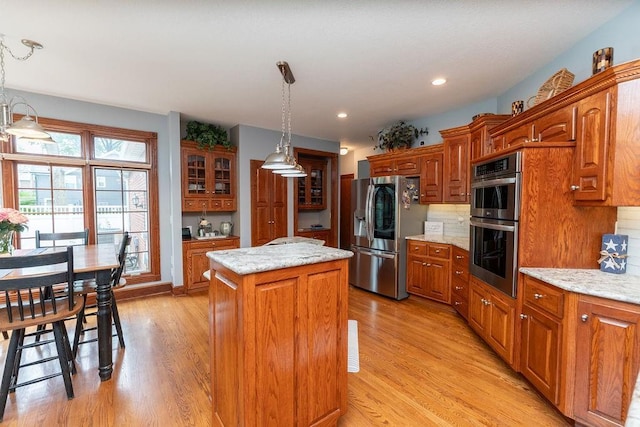 kitchen with a kitchen island, appliances with stainless steel finishes, hanging light fixtures, light stone countertops, and light wood-type flooring