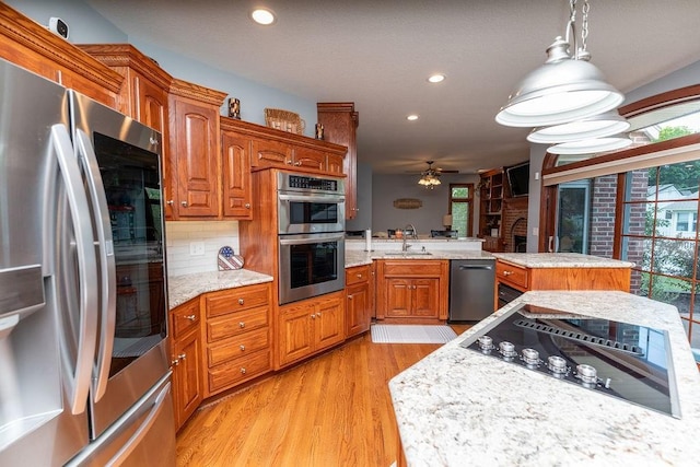 kitchen with a kitchen island, appliances with stainless steel finishes, sink, hanging light fixtures, and light hardwood / wood-style floors