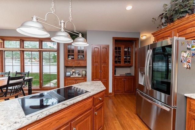 kitchen with stainless steel refrigerator, black electric stovetop, and light stone countertops