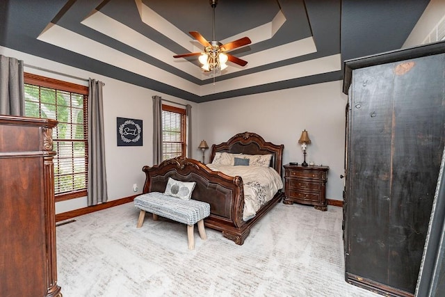 bedroom with ceiling fan, a tray ceiling, and light carpet