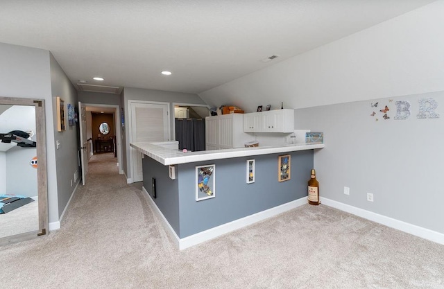 kitchen with lofted ceiling, white cabinetry, a kitchen bar, light carpet, and kitchen peninsula