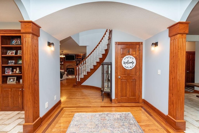 foyer entrance featuring ornate columns, lofted ceiling, a fireplace, and light wood-type flooring