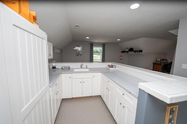 kitchen featuring white cabinetry, lofted ceiling, sink, and kitchen peninsula