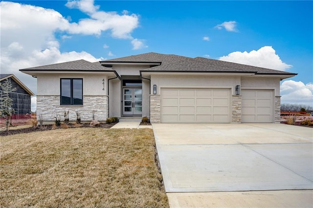 prairie-style home featuring a front lawn, stucco siding, a garage, stone siding, and driveway