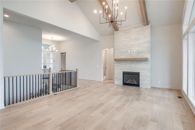 unfurnished living room featuring a notable chandelier, high vaulted ceiling, light wood-style flooring, a tiled fireplace, and baseboards