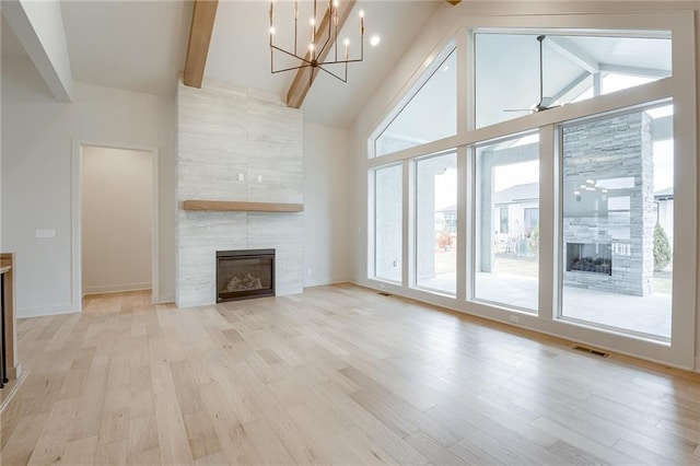 unfurnished living room featuring high vaulted ceiling, light wood-style flooring, a tiled fireplace, beamed ceiling, and ceiling fan with notable chandelier