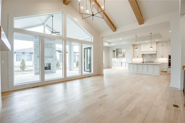 unfurnished living room featuring visible vents, high vaulted ceiling, beam ceiling, a fireplace, and light wood-style floors