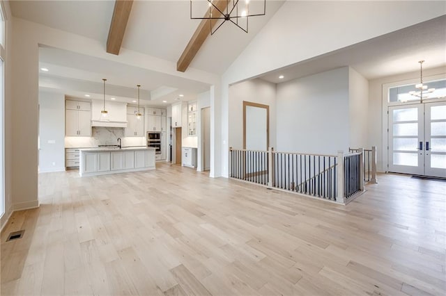 unfurnished living room featuring visible vents, an inviting chandelier, beam ceiling, light wood-style floors, and french doors