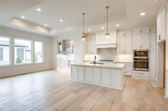 kitchen featuring a sink, a tray ceiling, light wood-style flooring, and stainless steel appliances