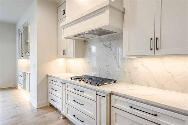 kitchen featuring premium range hood, light wood-style flooring, light stone counters, decorative backsplash, and stainless steel gas cooktop