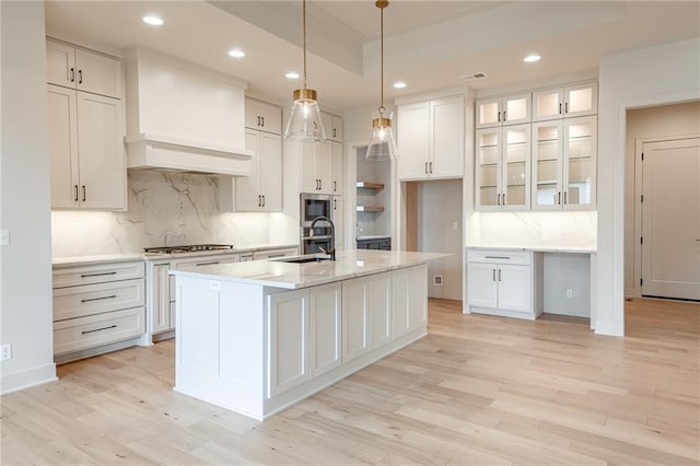 kitchen featuring light wood finished floors, white cabinets, an island with sink, and a sink