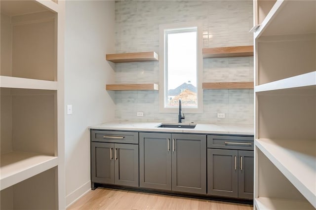 kitchen with open shelves, gray cabinetry, backsplash, and a sink