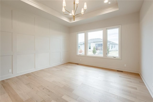 spare room with visible vents, light wood-style floors, a decorative wall, a raised ceiling, and a chandelier