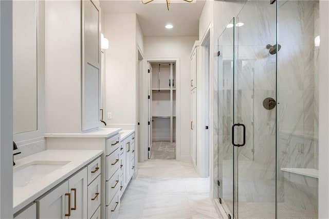 bathroom featuring a walk in closet, two vanities, marble finish floor, a stall shower, and a sink