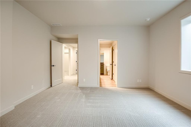 unfurnished bedroom with visible vents, light colored carpet, ensuite bathroom, and baseboards