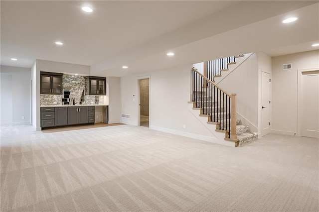 unfurnished living room with visible vents, stairway, light carpet, recessed lighting, and a sink