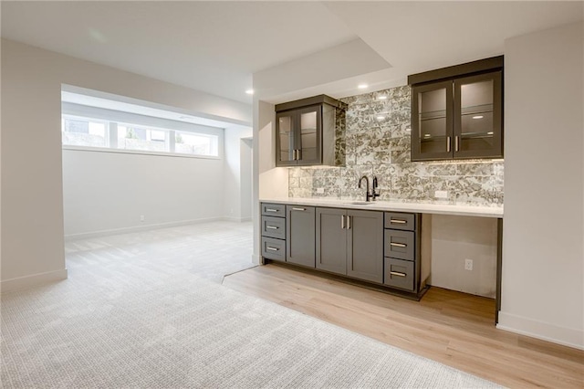 bar with baseboards, decorative backsplash, light wood-style flooring, wet bar, and a sink