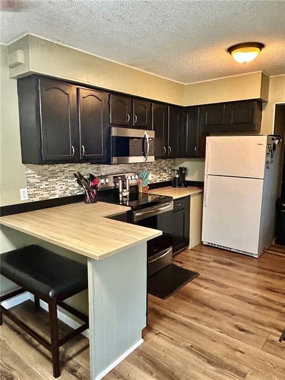 kitchen with kitchen peninsula, light hardwood / wood-style floors, a textured ceiling, a kitchen bar, and appliances with stainless steel finishes