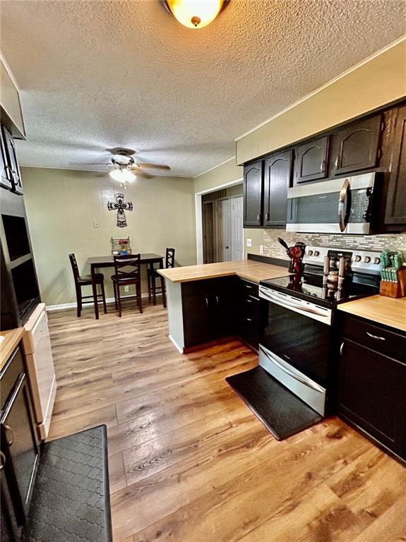 kitchen featuring backsplash, a textured ceiling, appliances with stainless steel finishes, dark brown cabinets, and light hardwood / wood-style floors