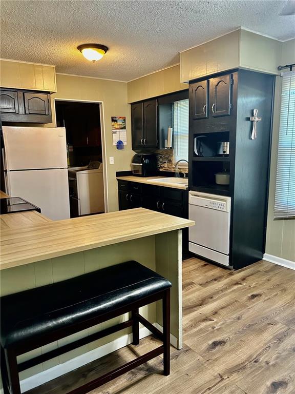 kitchen with white appliances, sink, light wood-type flooring, a textured ceiling, and kitchen peninsula